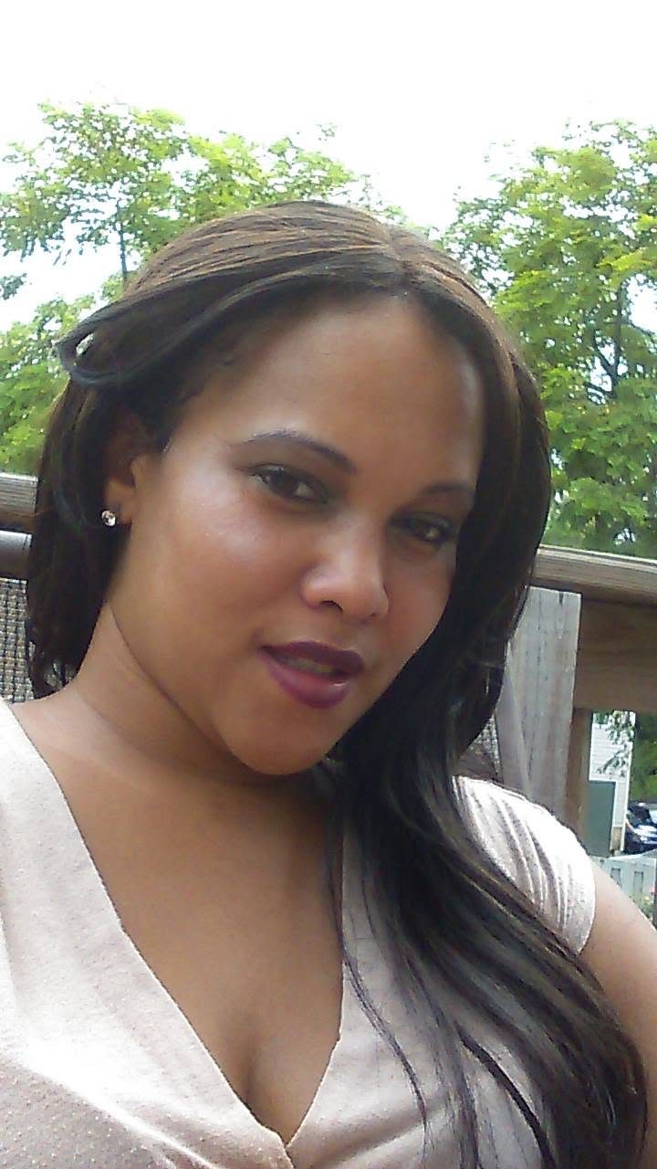 Teola Blake smiling, outdoors on a deck with green trees behind her.